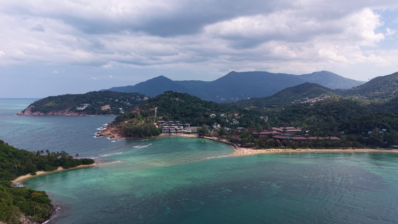 Aerial orbit capturing tropical bay with exposed sandbank linking island and mainland coastline