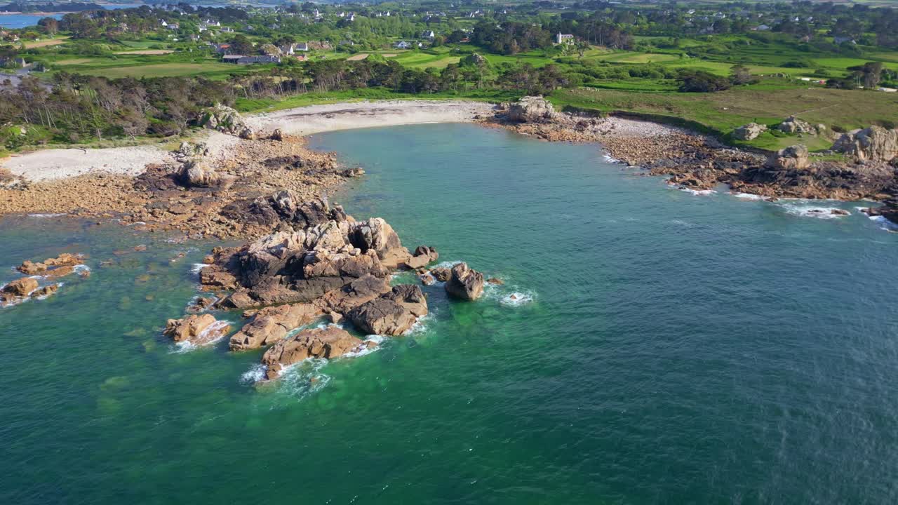 Aerial view from above the sea toward the rocky shore, beaches, and coastal vegetation of the Pink Granite Coast.