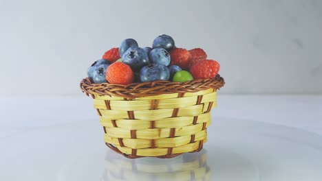 rotating wooden basket with different forest berries close-up on a white wooden table. 4k slow motion loop raw video.