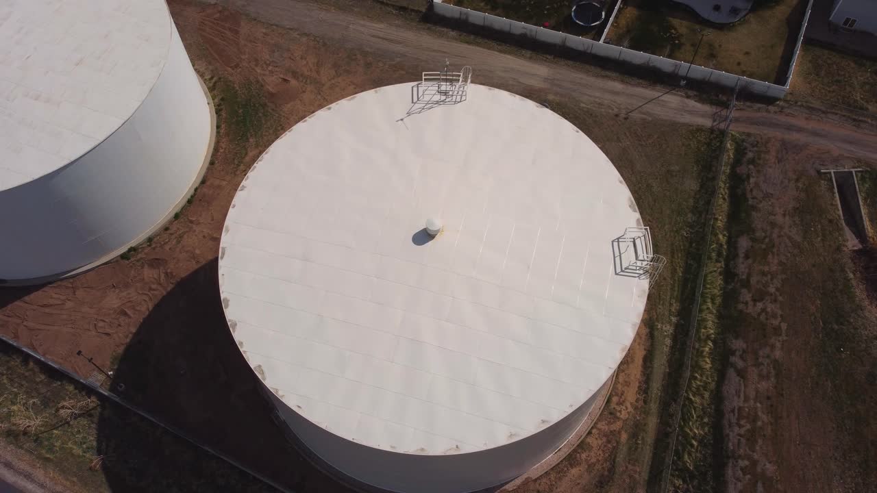 Slow flying overhead drone shot of a couple of small white local city community water towers in suburban rural neighborhood on sunny spring summer day. In 4k real time.