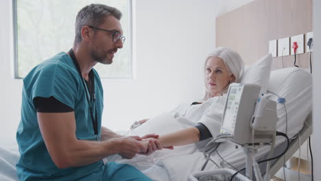 male nurse taking mature female patients blood pressure in hospital bed with automated machine