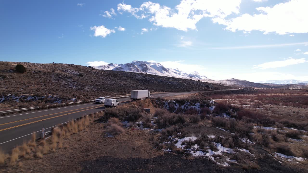 coches y camiones conduciendo rápido en la carretera de sierra nevada con paisaje de montañas nevadas en imágenes aéreas de fondo