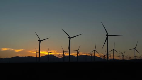 silhouettes of wind turbines with sunset skyline in background, green energy concept, static shot