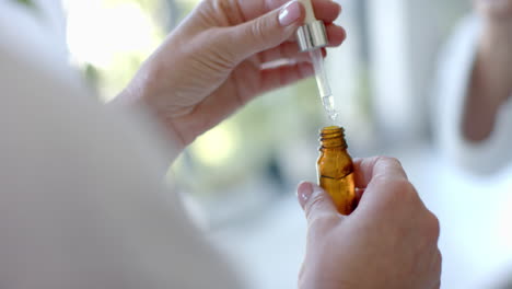 using dropper to add liquid into bottle, mature woman preparing essential oils