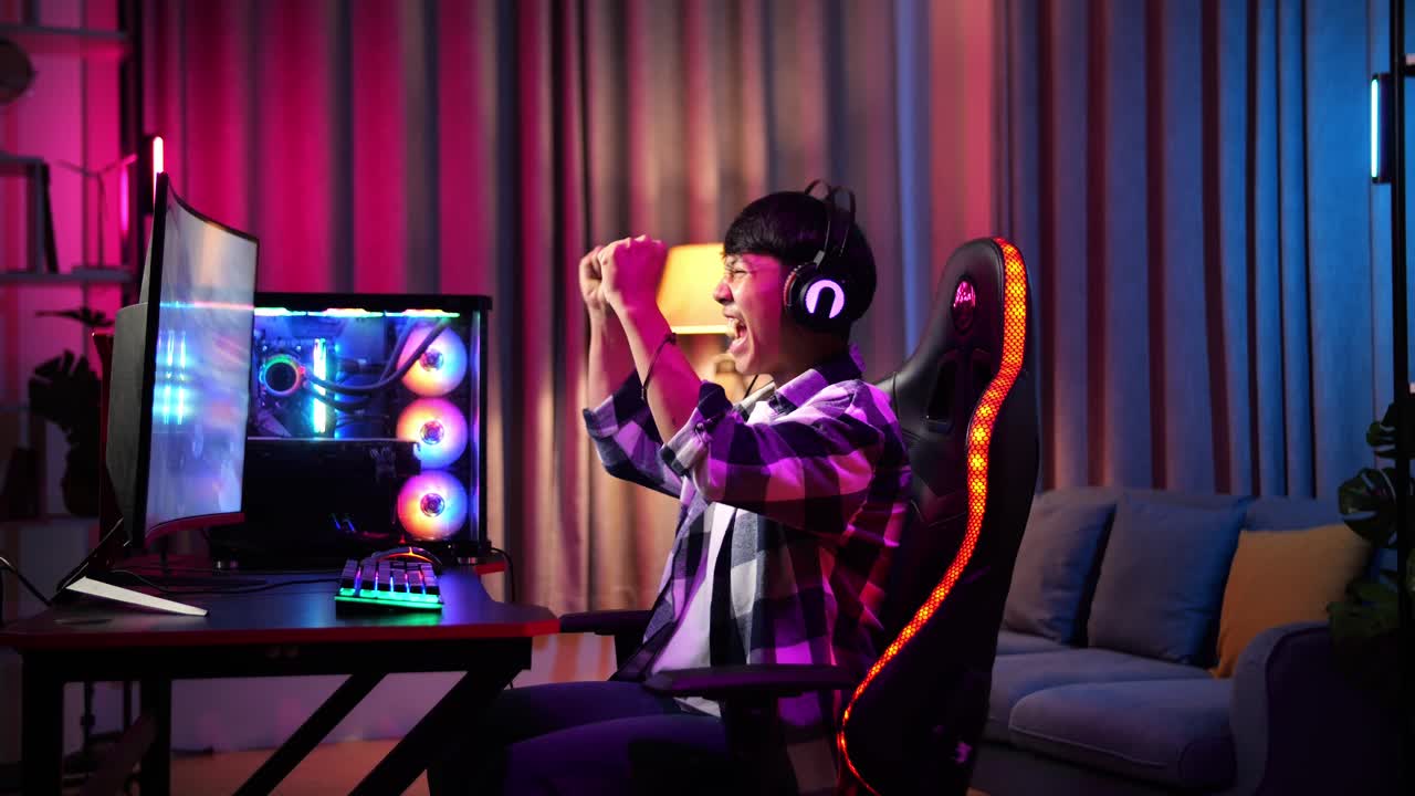 un adolescente asiático emocionado celebra la victoria mientras juega videojuegos en la computadora.