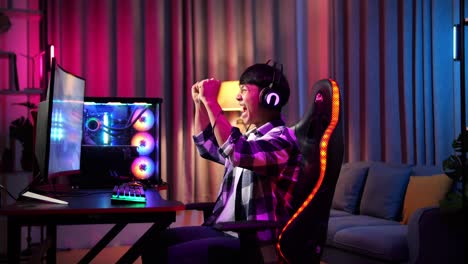 excited asian teen boy gamer celebrates victory while playing video game on computer