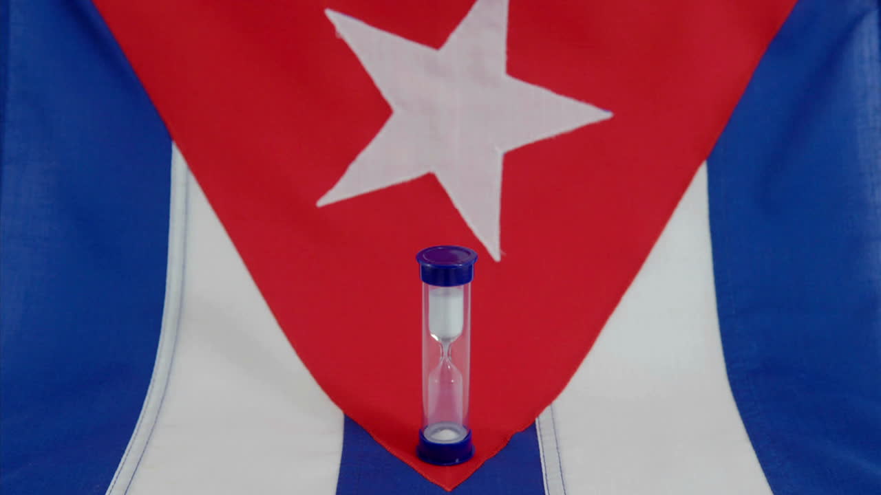una bandera cubana se encuentra debajo de un reloj de arena