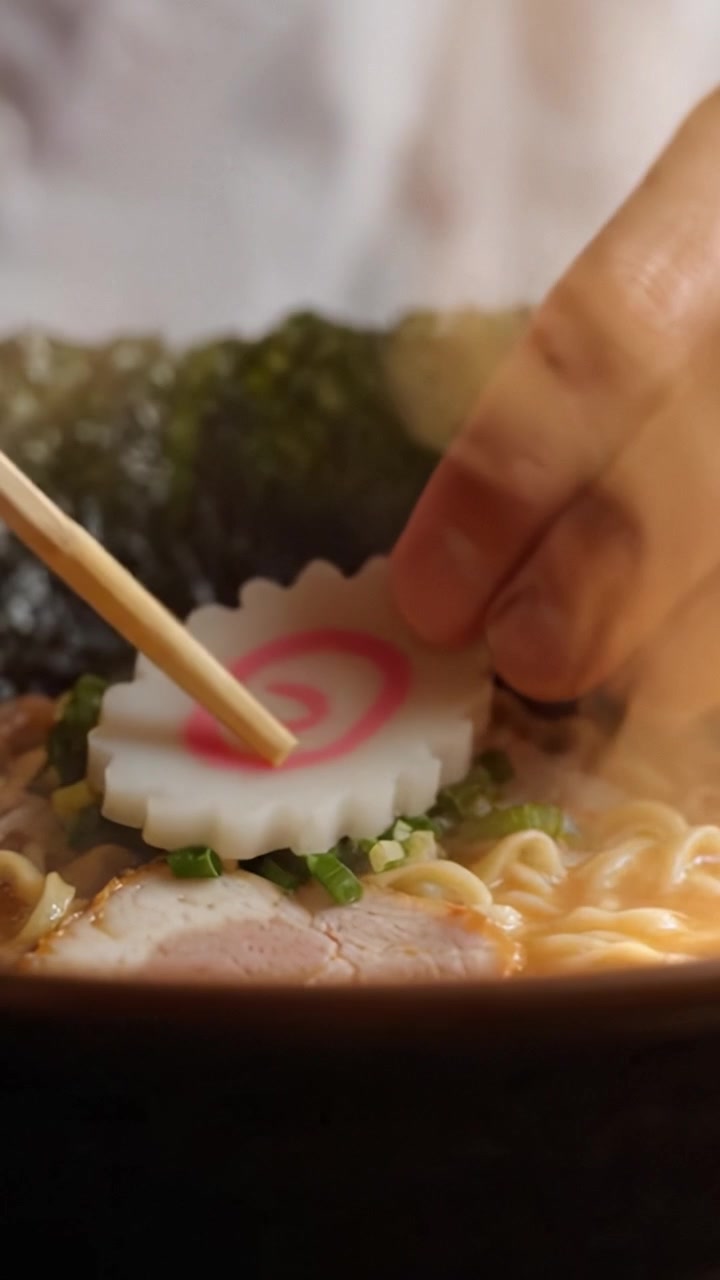 Assaporando deliziosi ramen: una vista ravvicinata di noodles, condimento e brodo con una presentazione artistica di kamaboko decorativo e cipollotti.