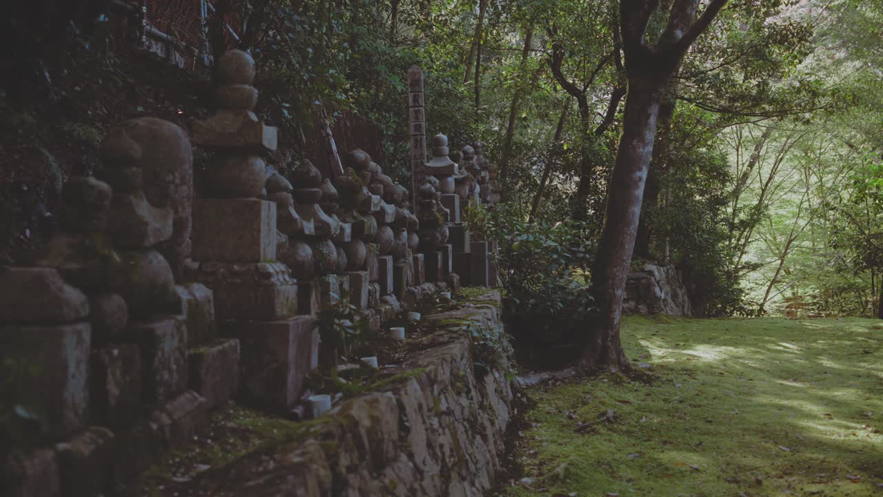 A tranquil scene of Japanese stone markers set amidst a lush forest in Takaosan, Japan. Soft afternoon sunlight filters through the trees, creating a serene and mystical atmosphere.