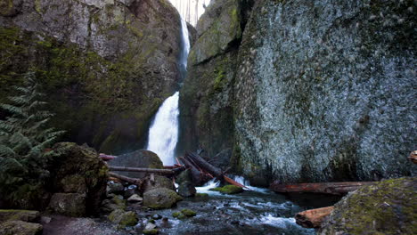 a drone low towards the river moving closer to wahclella falls with fallen tree logs all around