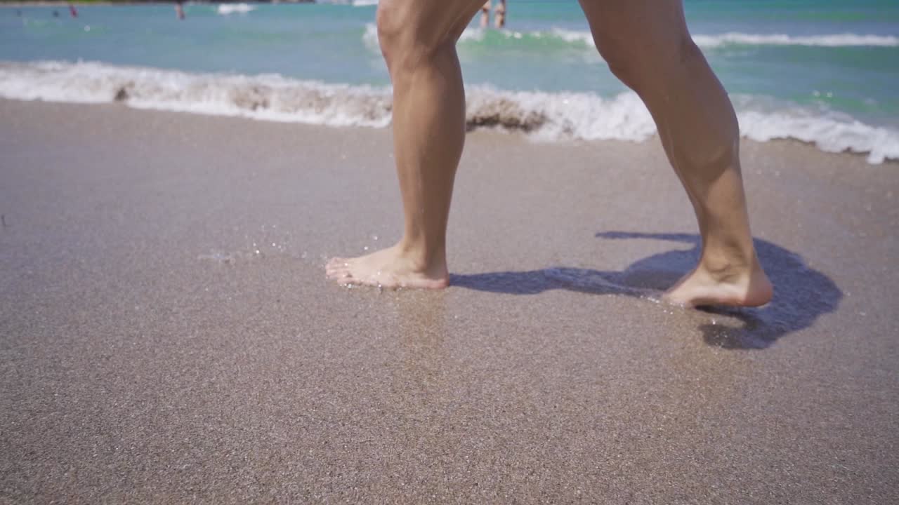 Giovane uomo che corre a piedi nudi in spiaggia, al rallentatore