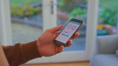 primer plano de un hombre en casa con el teléfono mirando una aplicación de seguimiento de fitness