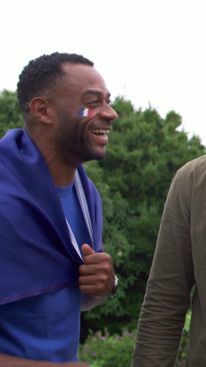 Video verticale: Uomo che parla con maglietta blu tira una bandiera, indicando un amico in giardino, vernice tricolore