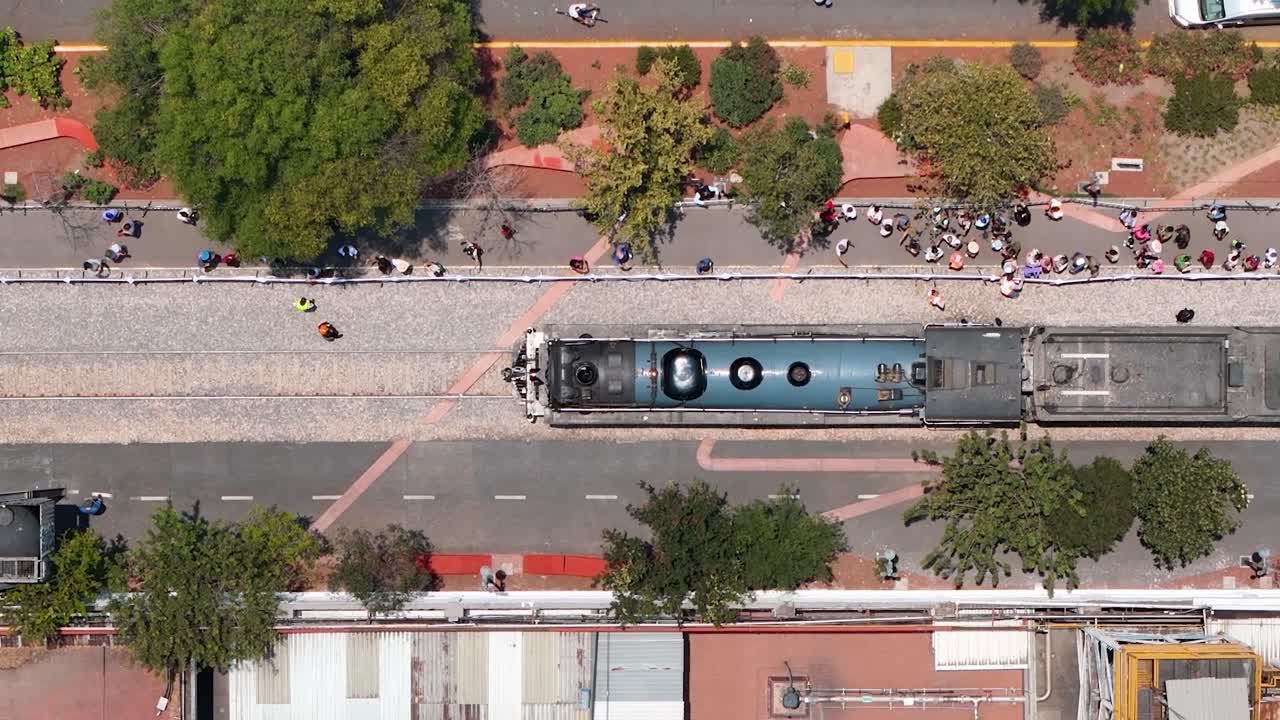 Aerial view of a train on tracks with people walking alongside in an urban area