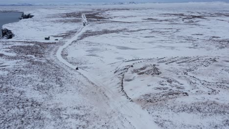 Person-on-quad-bike-driving-through-vast-open-snow-covered-Iceland-landscape,-aerial