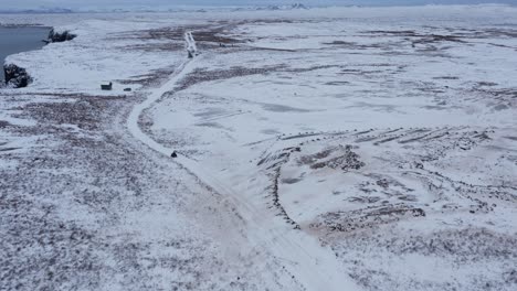 person on quad bike driving through vast open snow covered iceland landscape, aerial