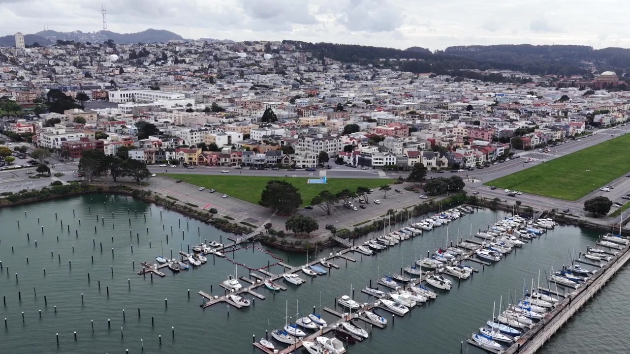 Lukemattomat purjeveneet täyttävät San Franciscon Marina Districtin satamalaiturit, pastellinväriset rivitalot ja vihreä puisto levittäytyvät sumuisille rinnemaisemille pilvisen taivaan alla. Lähestyvä ilmakuva dronella.