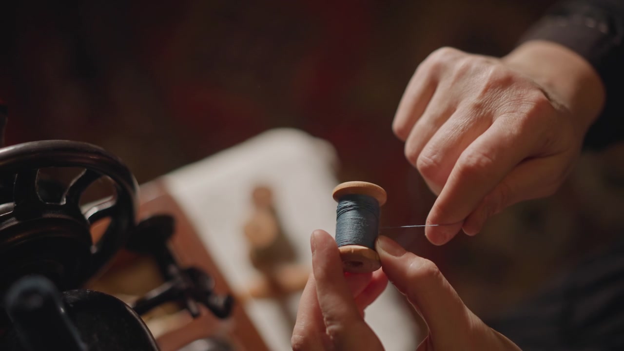 Scatto dettagliato di mani con apparecchio da cucito. Primo piano di dita che guidano il filo in un dispositivo da cucito vintage. Vista intima di mani che posizionano la bobina accanto a una macchina da cucire a pedale antica.