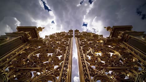 a video still of ornate golden gates opening towards a bright sky, viewed from a low angle