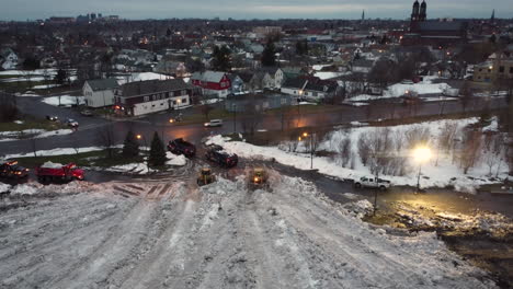 Vista-Aérea-Ascendente-De-Equipo-Pesado-Moviendo-Nieve-Cerca-De-Una-Calle-Concurrida-De-La-Ciudad-Al-Atardecer