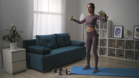 smiling woman dressed sportswear is training with small dumbbells in living room home workout for good shape of body sportswoman is lifting weights