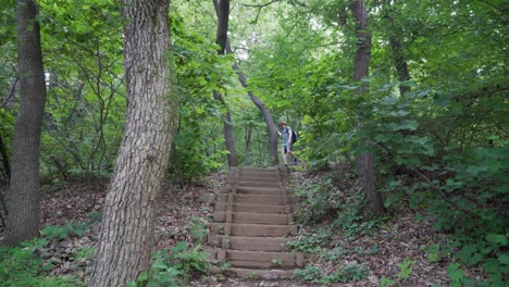 European-tourist-hiker-walks-down-the-wooden-stairs-following-trail-path,-forest-frees-background-wide-angle-view