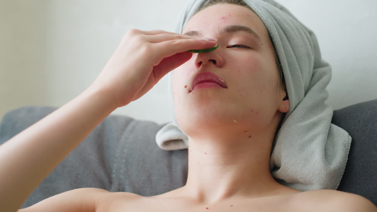 Young girl feeling relaxed while rubbing cucumber all over her face, enjoying a calming skincare routine, towel wrapped around her head, enhancing the peaceful atmosphere