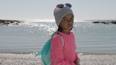 portrait of little girl on beach turning looking wearing backpack beanie pink clothes