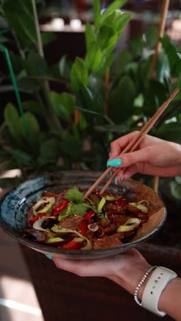 woman eating beef stir-fry with chopsticks