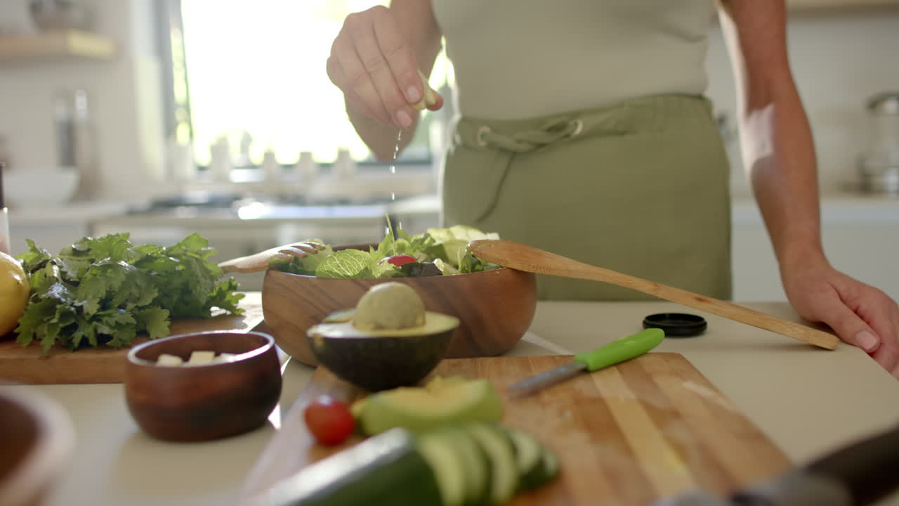 Caucasian woman preparing salad in kitchen, holding wooden spoon