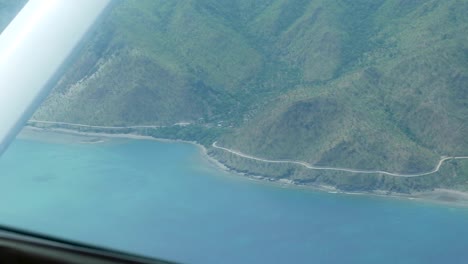 flying on stunning coastline with winding road, hills and turquoise water ocean in a small plane on remote tropical island timor leste, southeast asia