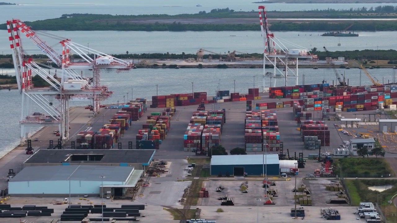 Port of Tampa container yard with gantry cranes and cargo ship beside channel, aerial tracking right backdrop