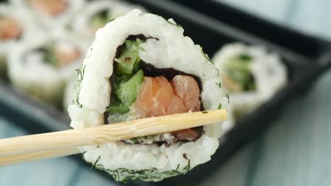 close up of salmon sushi roll with chopsticks