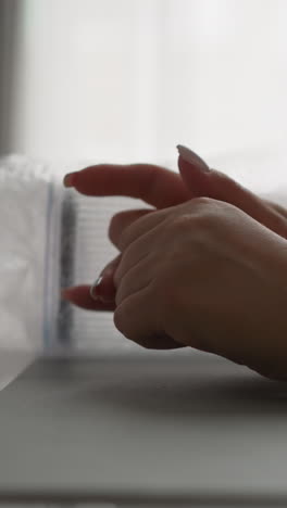 female hands with neat manicure lie on kitchen table with new transparent containers. young woman kneads fingers nervously sitting by window