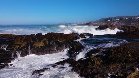 Slow-motion-aerial-of-wave-crashing-over-rugged-rocks-on-coastline