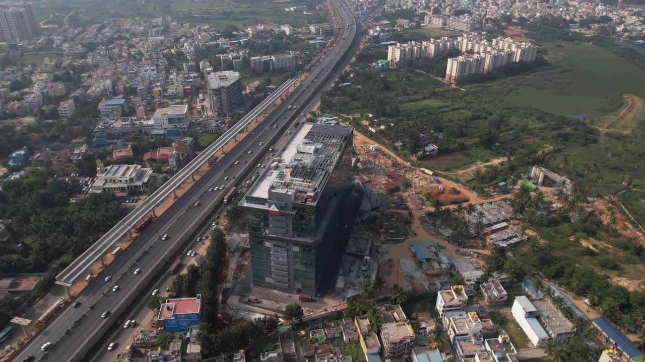 Riprese aeree di un'autostrada indiana in rapida espansione, con una strada di servizio, automobili in rapido movimento ed edifici commerciali e residenziali