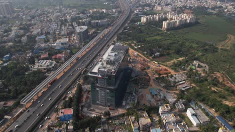 aerial footage of an indian highway that is expanding quickly, with a service road, fast-moving automobiles, and commercial and residential buildings