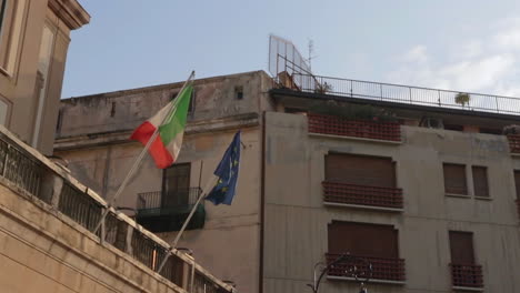 italian and eu flag fluttering in wind from poles attached to balcony, italy