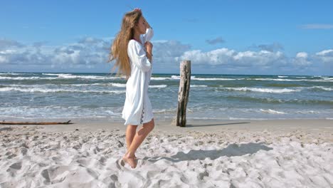 a woman standing in the sand at the ocean beach enjoying the blowing of the wind and touch her long hair and her dress to relax