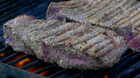 two juicy rib eye steaks cooking on the grill as fire and flames shoot up down below