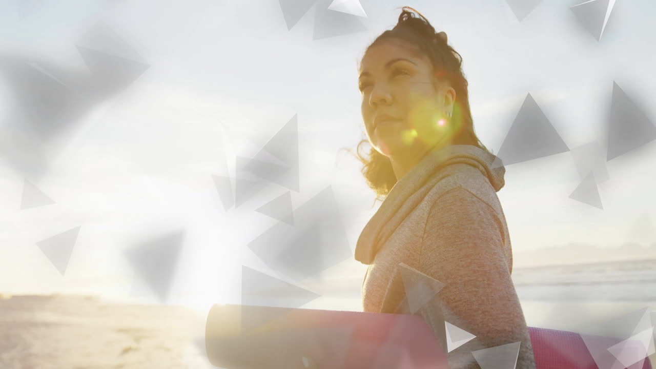 Woman holding yoga mat with geometric shapes animation over beach background