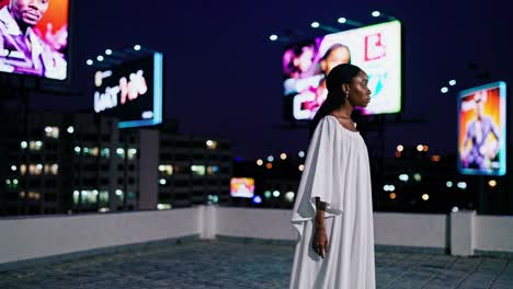 young woman in a white dress is standing on a rooftop at night, surrounded by large illuminated billboards displaying various advertisements, with the city lights twinkling in the background
