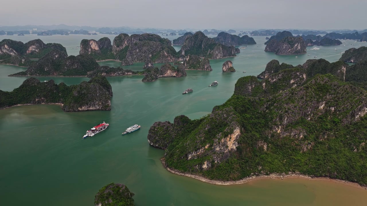 Ha Long Baai, Vietnam: Brede dolly-in luchtopname van kalkstenen karst-eilanden en toeristische cruiseschepen op smaragdgroen water.
