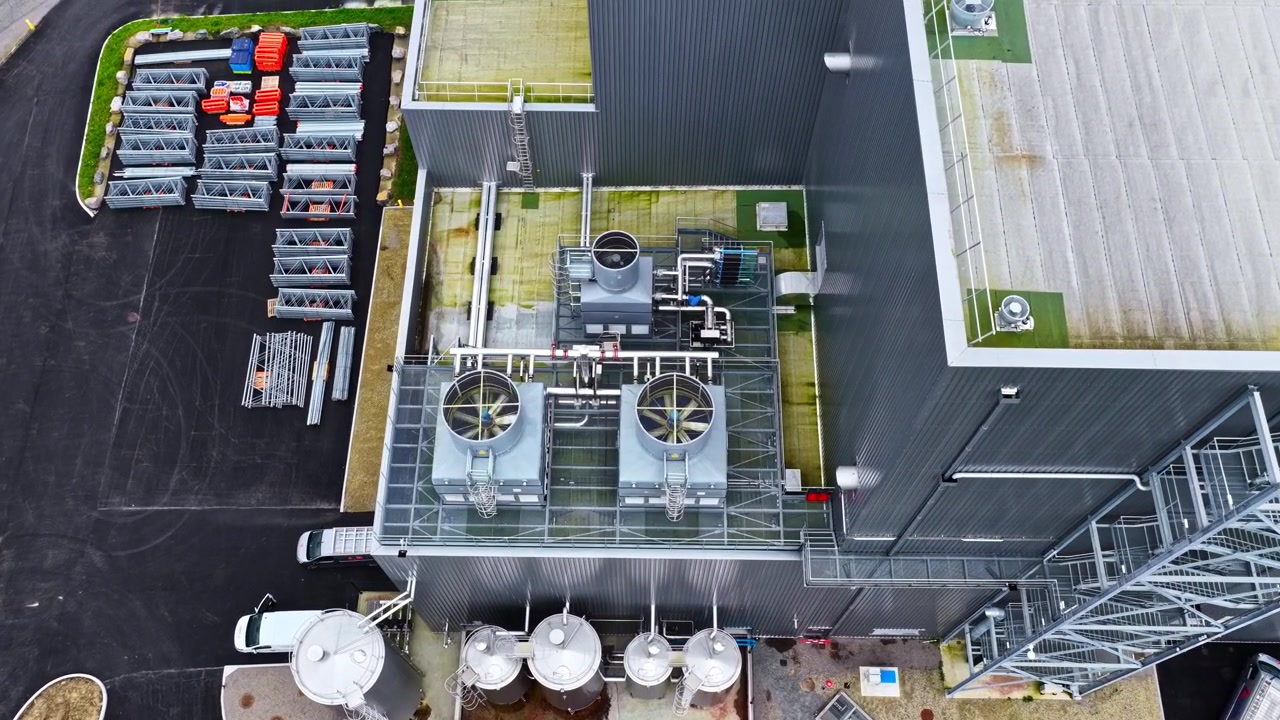 Un impianto industriale presenta unità di raffreddamento sul tetto e grandi serbatoi di stoccaggio. Ideale per processi industriali o temi di produzione.