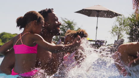 family on summer holiday with two girls in swimming pool splashing mother