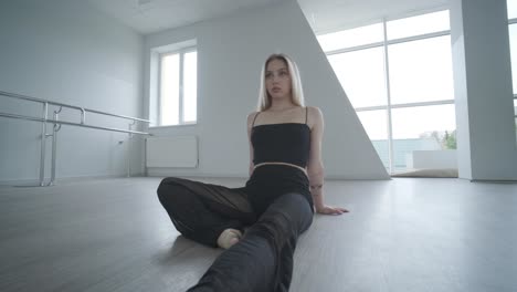 fit girl in black clothes performing contemporary. female dancer shows flowing motions, body and hands waves at white room. modern ballet dance choreography. young woman is moving smoothly