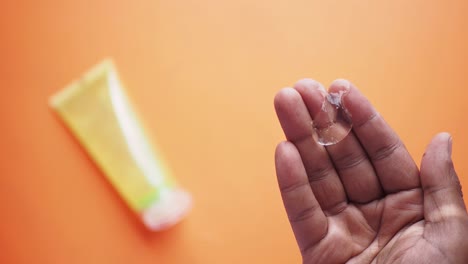 la mano sosteniendo un tubo de gel de aloe vera sobre un fondo naranja