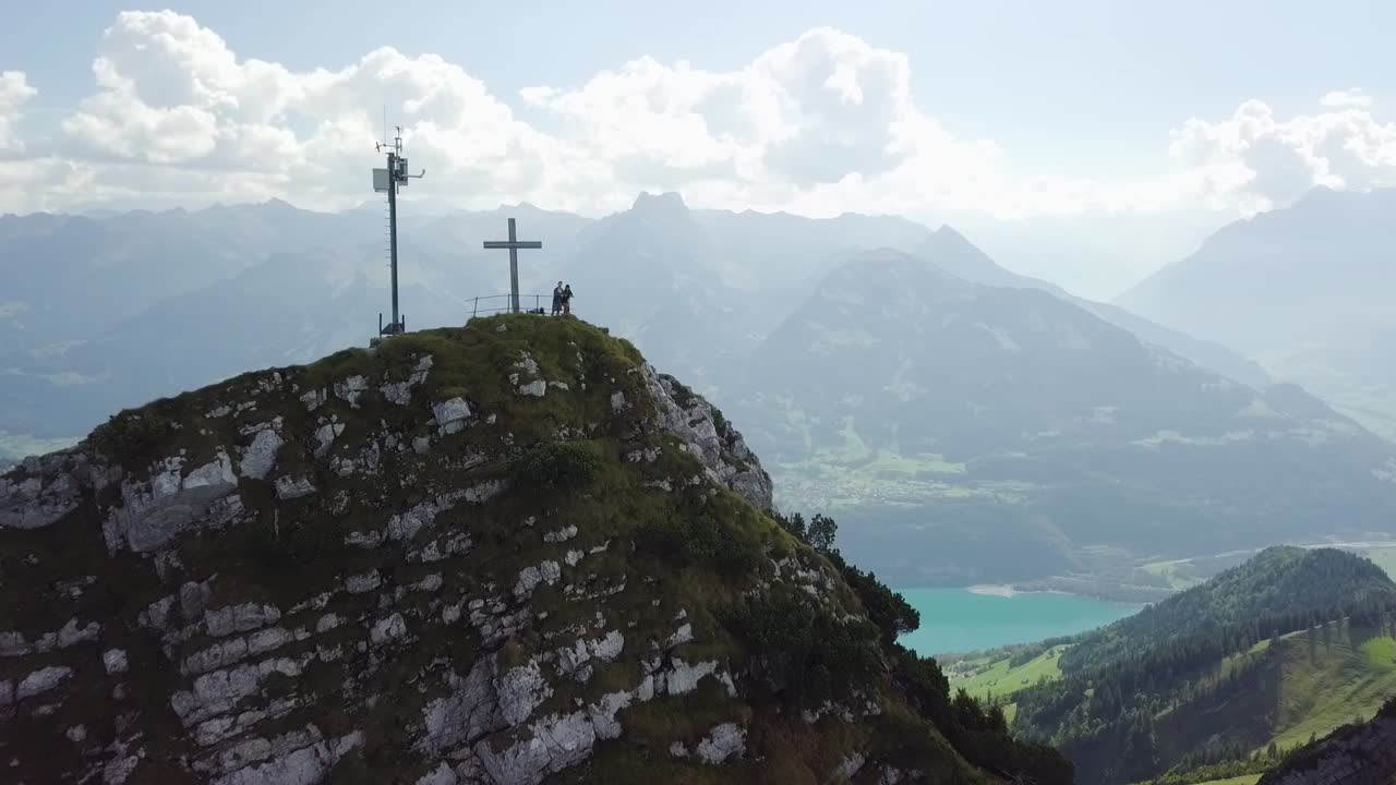드론은 정상 십자가 옆에 서 있는 여성과 남성에게 가까이 뒤로 날아갑니다.