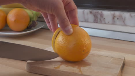 man's hand cut orange fruit in half on wooden chopping board