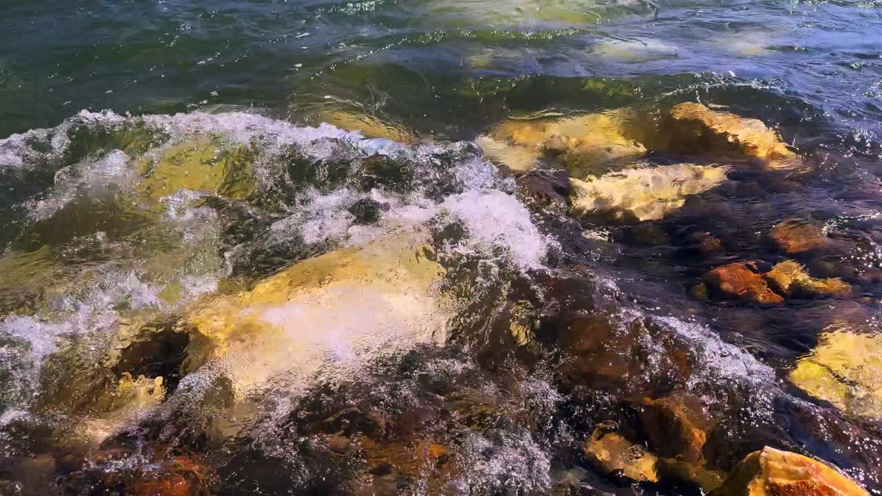 A Tranquil Coastal Scene Capturing the Dance of Waves Over Colorful Rocks and Stones Beneath the Surface of the Clear, Glimmering Water